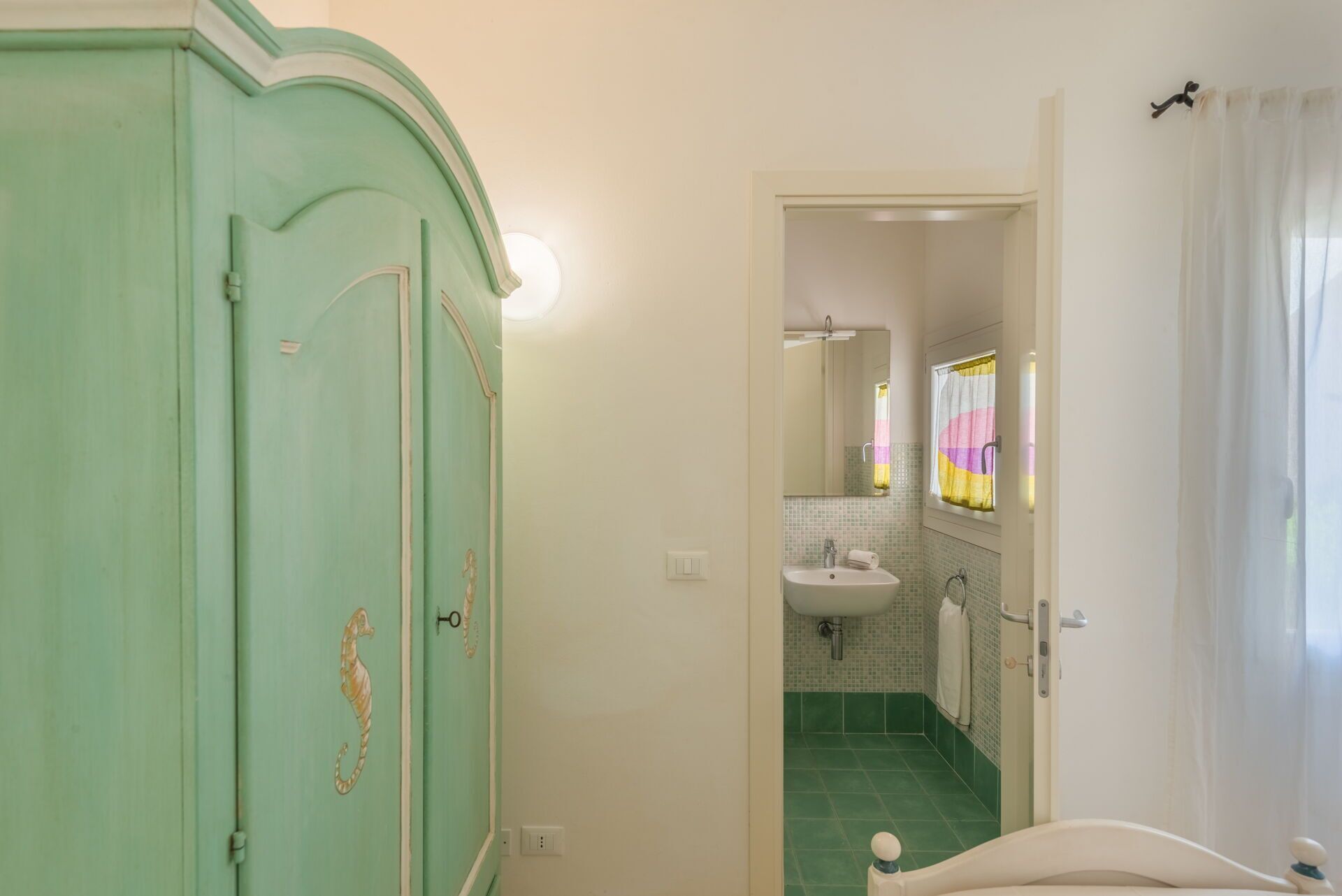 Un baño con piso de baldosas verdes, un lavamanos blanco y un espejo encima.