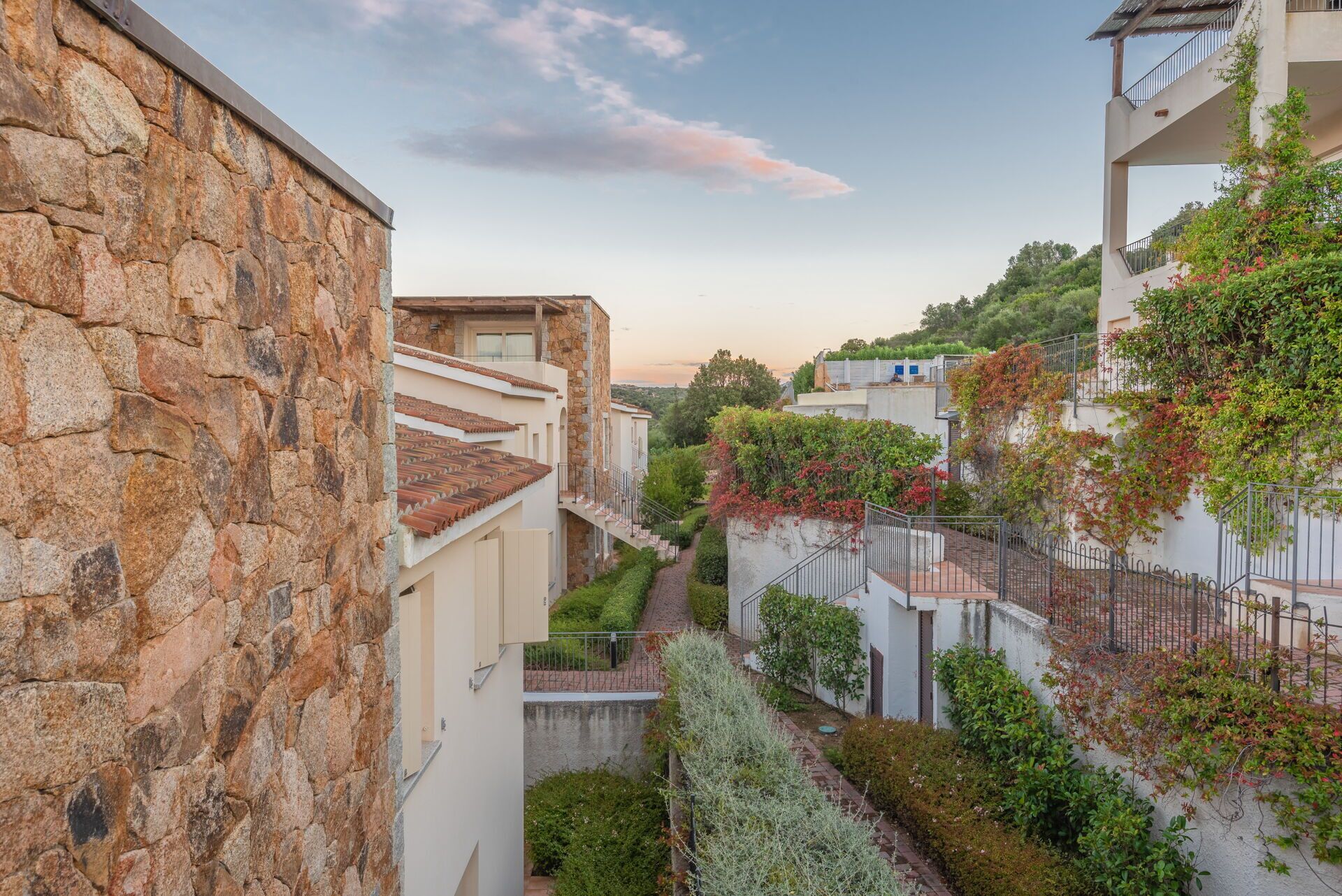 Una calle estrecha con edificios de piedra, un camino pavimentado y vegetación.