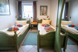 Una habitación con dos camas de madera verde, una mesita, una ventana con cortinas y un cuadro en la pared.