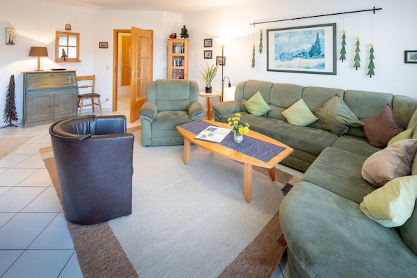 Una sala de estar con sofá, sillón, mesa de centro y una pequeña estantería.