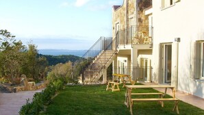 A two-story building with a stone facade, a balcony, and a staircase leading to the upper floor. There are picnic tables on the lawn. - Baia Bianca Albatros Apartment Sardinia (Baja Sardinia)