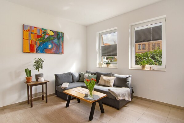 Una sala de estar con sofá, mesa de centro, un cuadro y ventana con vistas.