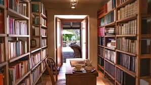 Une bibliothèque avec des étagères de chaque côté, une table en bois avec une chaise, et une vue sur un espace extérieur aménagé en patio.