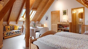 A cozy attic bedroom with a wooden ceiling, a sofa, a desk, and a bed.