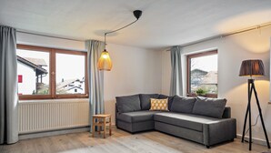 A modern living room with a sectional sofa, a small wooden stool, a floor lamp, and a radiator. - Holiday Apartment 'Silvia' with Mountain View, Shared Garden, and Wi-Fi (Rosshaupten)