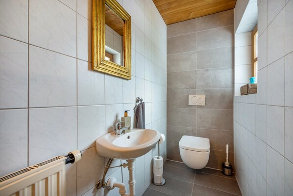 Une salle de bain avec un lavabo blanc, des toilettes, un miroir et un radiateur.