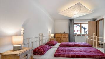 Camera da letto con due letti, una cassettiera in legno, un comodino, una lampada e vista su un edificio dalla finestra.