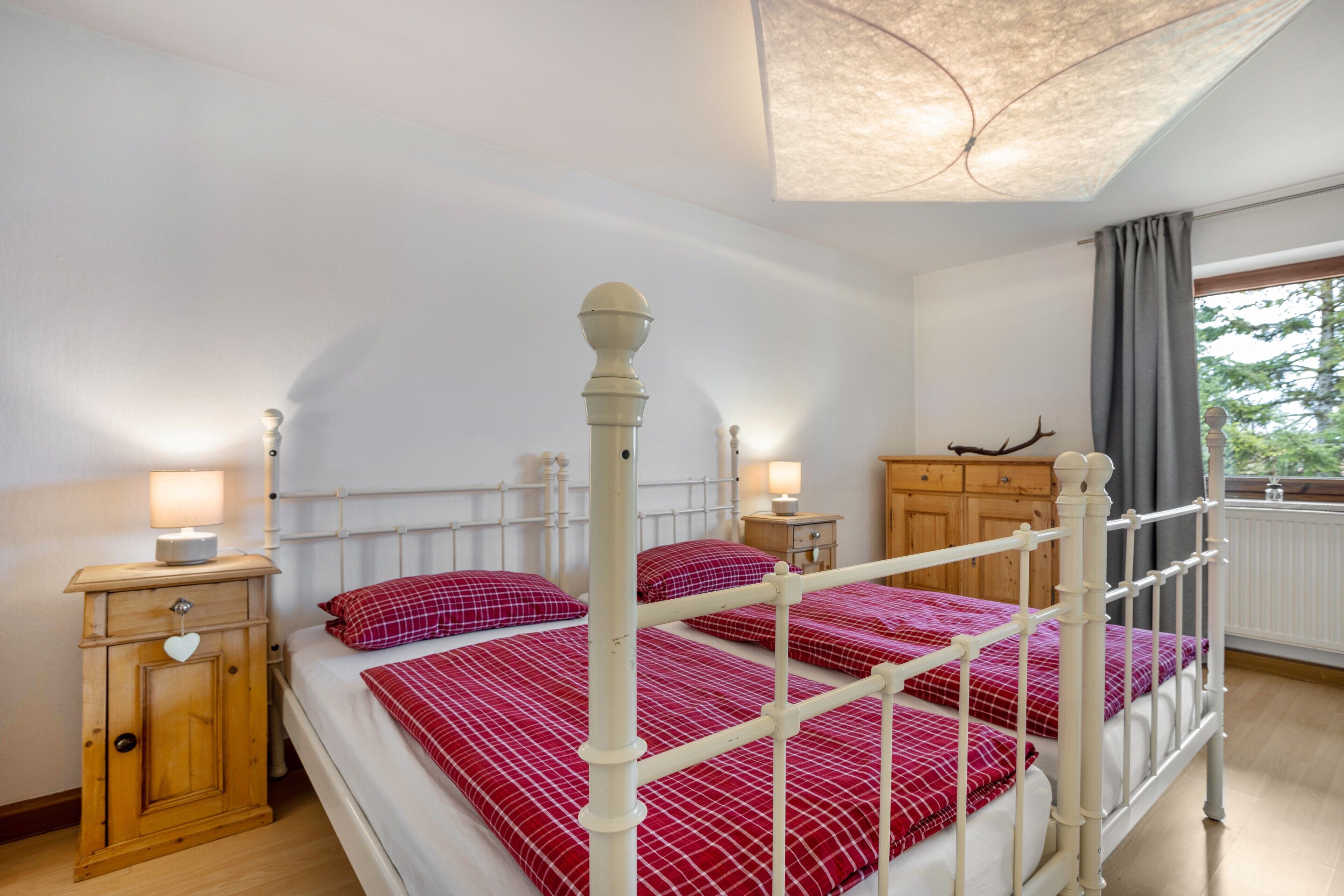 Een slaapkamer met een hemelbed, houten nachtkastjes, een kaptafel en een raam met gordijnen.