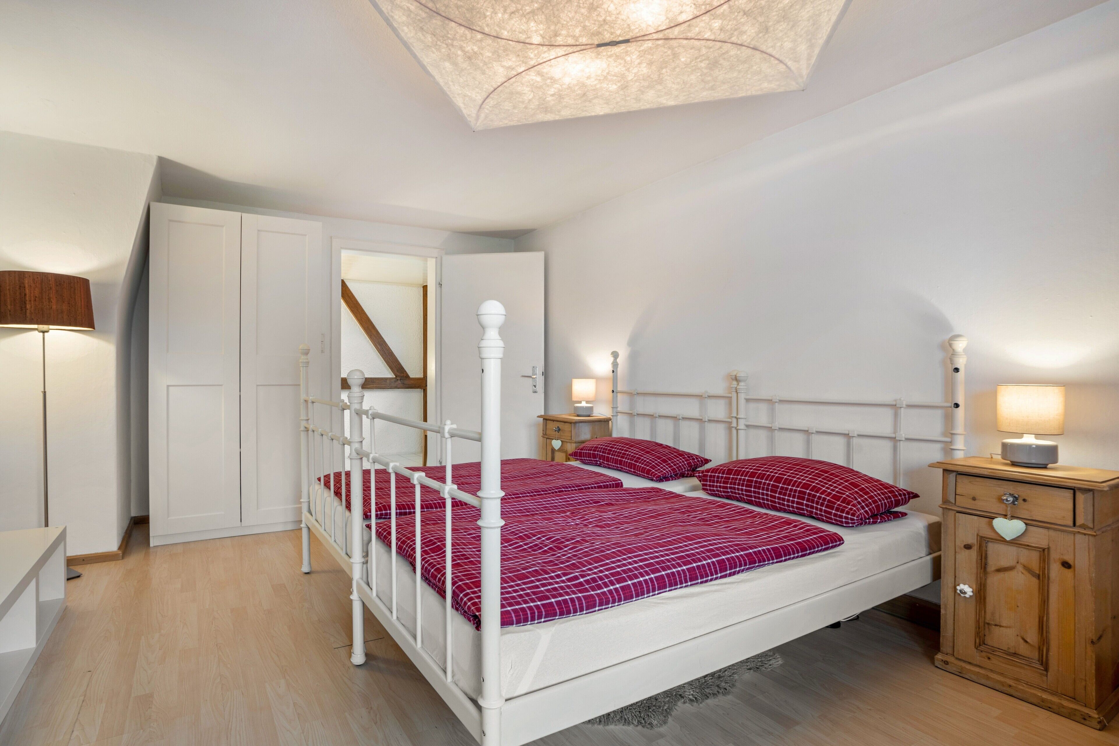 A bedroom with a four-poster bed, a wooden cabinet with a heart-shaped handle, and a ceiling light fixture.