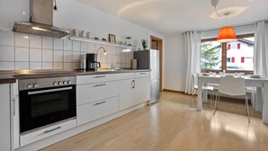 A modern kitchen with white cabinetry, a built-in oven, and a dining area with a table and chairs. - Holiday Apartment 'Silvia' with Mountain View, Shared Garden, and Wi-Fi (Rosshaupten)