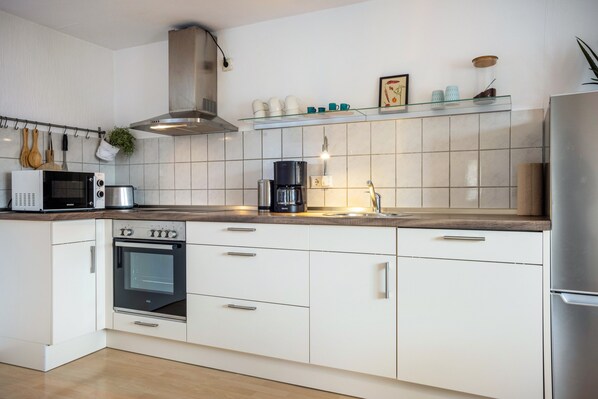 A modern kitchen with white cabinetry, a built-in oven, a microwave, a coffee maker, and a stainless steel range hood.