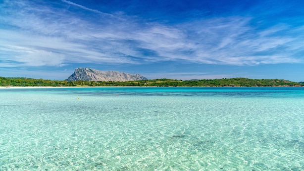 Un mar turquesa y transparente con una montaña al fondo y una playa a la izquierda.