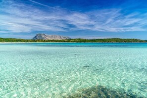 A clear turquoise sea with a mountain in the background and a beach on the left.