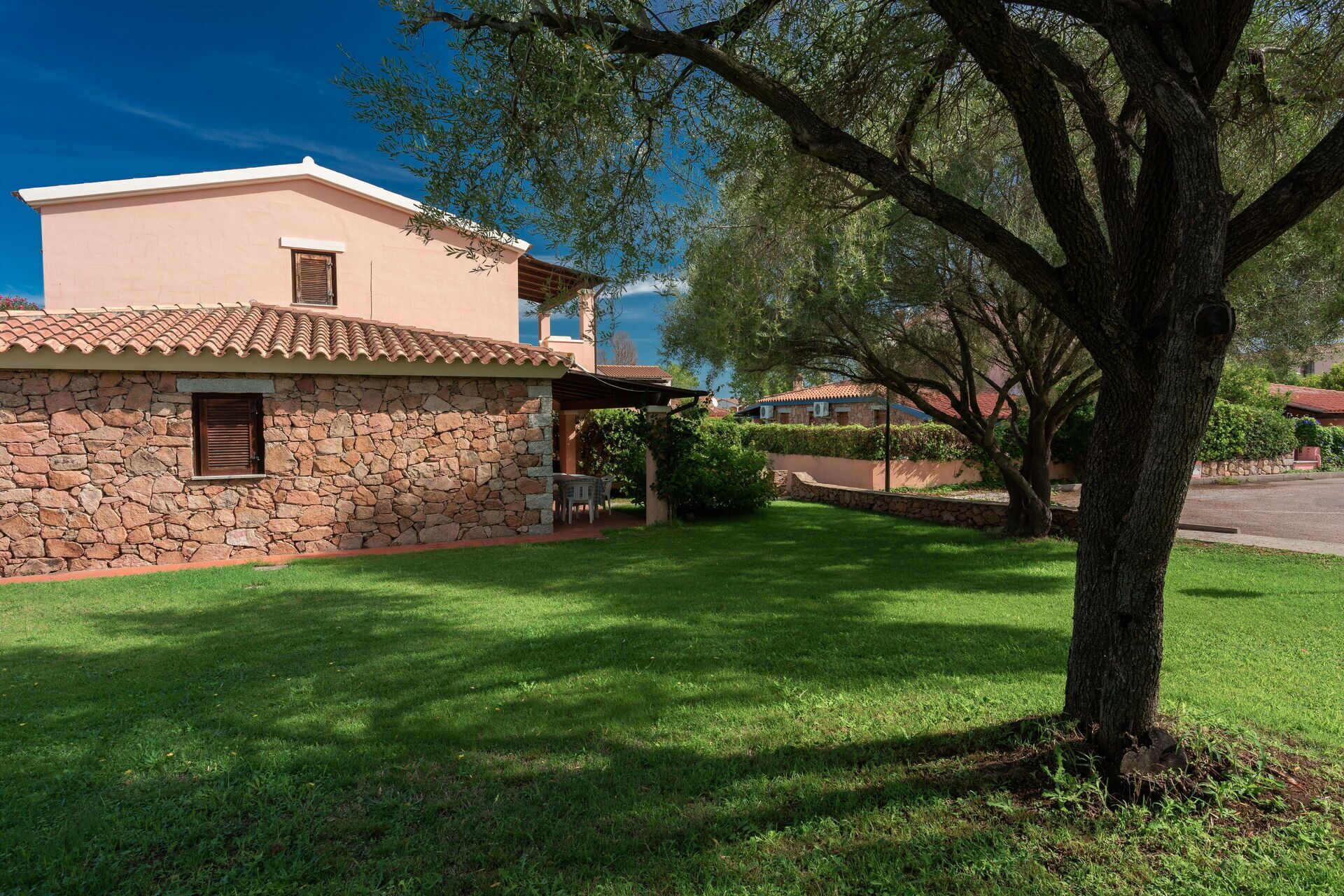 A stone building with a tiled roof, a well-maintained lawn, and a large tree in the foreground.