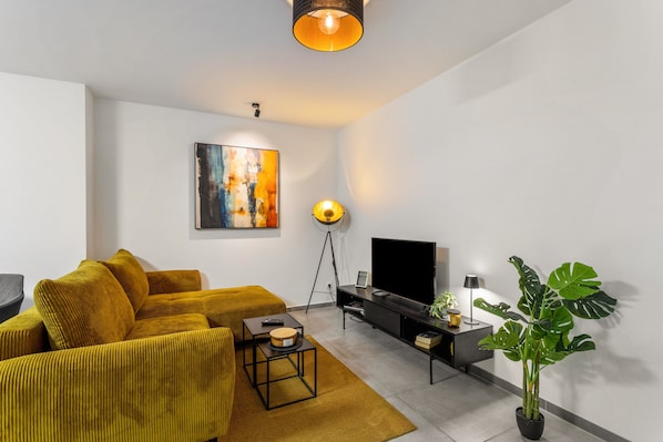 Una sala de estar moderna con un sofá, un televisor, una lámpara de pie, un cuadro y una planta en maceta.