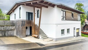 Ett modernt hus i två våningar med en inglasad veranda, en trätrappa och en liten trädgård framför huset.
