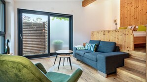 Un salon moderne avec un canapé, un fauteuil vert, une petite table ronde et un escalier en bois.