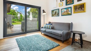 Ett vardagsrum med en grå soffa, ett litet svart bord, en blå, mönstrad matta och en stor skjutdörr i glas som leder ut till en uteplats.