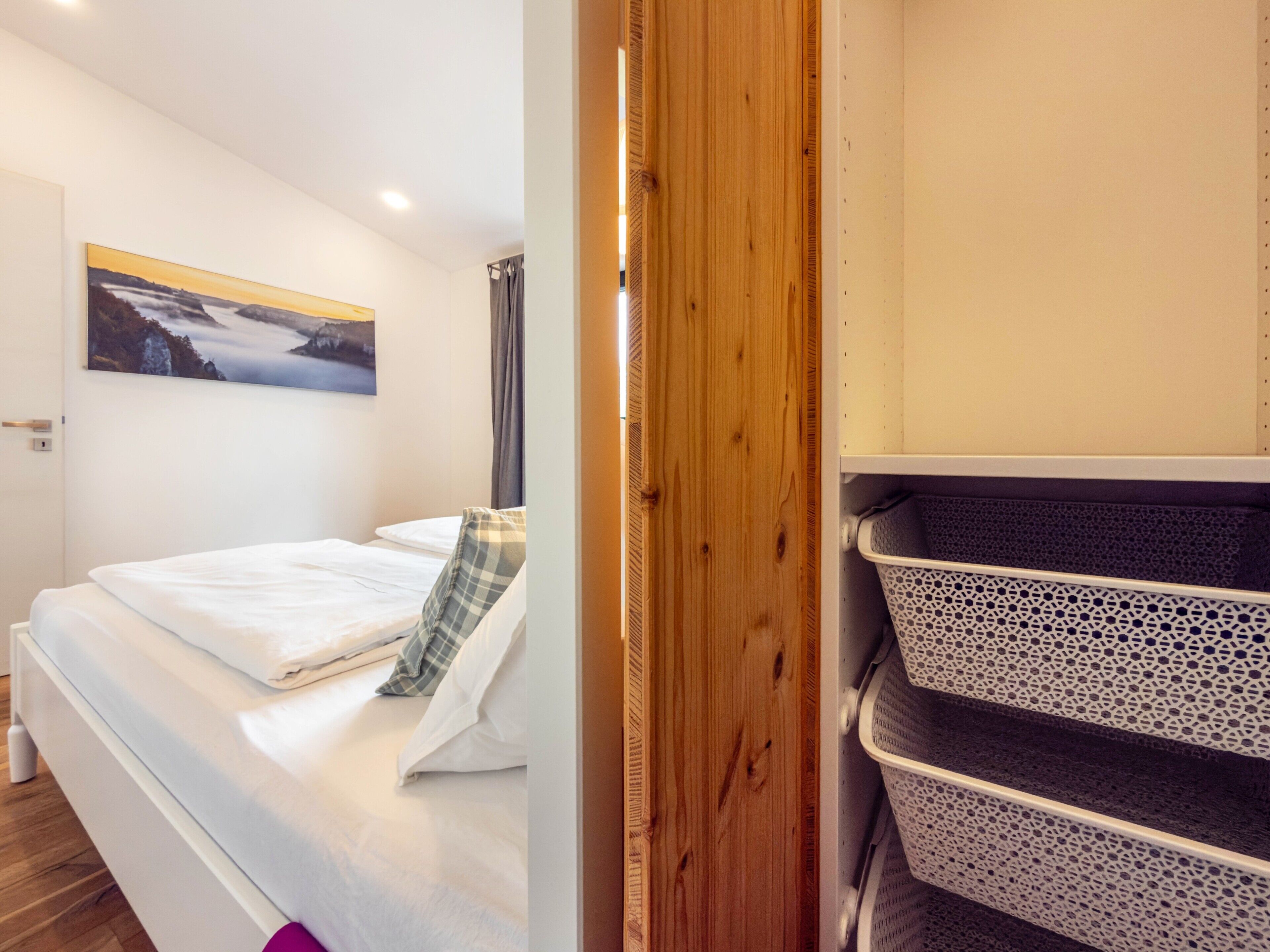 Een hotelkamer met een bed, een aan de muur bevestigd schilderij, een houten deur en een opbergunit met een gaasafdekking.