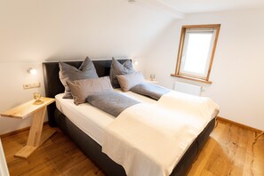 Un dormitorio con cama, mesitas de noche, una ventana y suelo de madera.