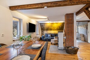 Una sala de estar moderna con chimenea, un comedor con mesa de madera dispuesta para cuatro personas y un rincón de estar acogedor con sofá y sillones.