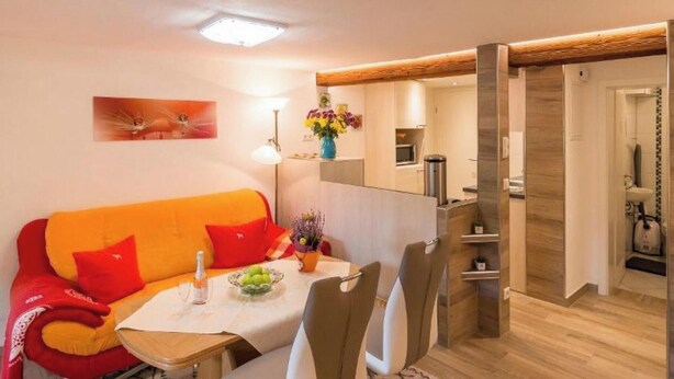 Een moderne woonkamer met een bank, eettafel, stoelen, een lamp en een keuken die zichtbaar is door een open deur.