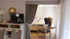 Een slaapkamer met een bed, een stoel, een bureau met een televisie en een spiegel.