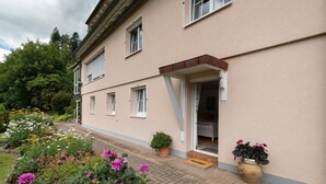 A two-story building with a paved entrance, potted plants, and a doormat. - Gartenblick Apartment with Private Terrace, Shared Garden and Wi-Fi (Enzklösterle)
