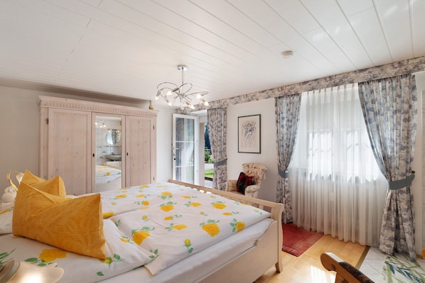 Un dormitorio con una cama, una silla, un espejo y una ventana con cortinas.