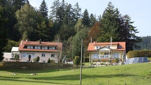 Una casa a due piani con tetto in tegole rosse, un balcone e pannelli solari nel giardino.