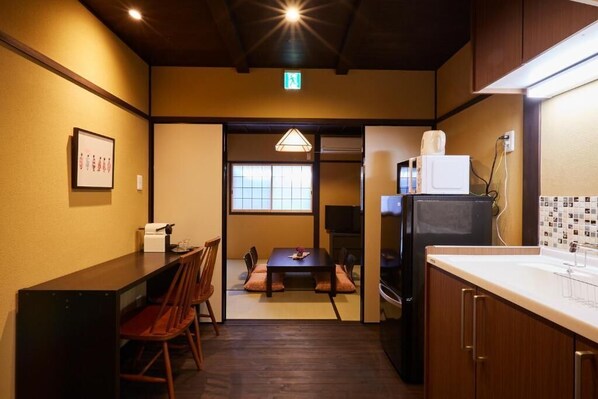 A compact kitchen with a dining area, wooden cabinets, a refrigerator, and a small TV. - Miro Matsubara Takaseigawa Tei North (Kyoto)
