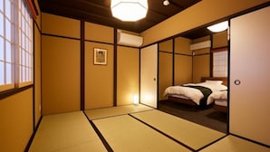 A traditional Japanese-style room with tatami flooring, a bed with a white comforter, an air conditioning unit, and a hanging light fixture.