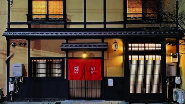 A traditional Japanese building with a tiled roof, wooden lattice windows, and a red awning.