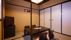 A traditional Japanese-style room with tatami flooring, a low table with chairs, a television, and sliding shoji doors.