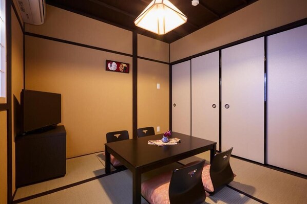 A traditional Japanese-style room with tatami flooring, a low table with chairs, a television, and sliding shoji doors.