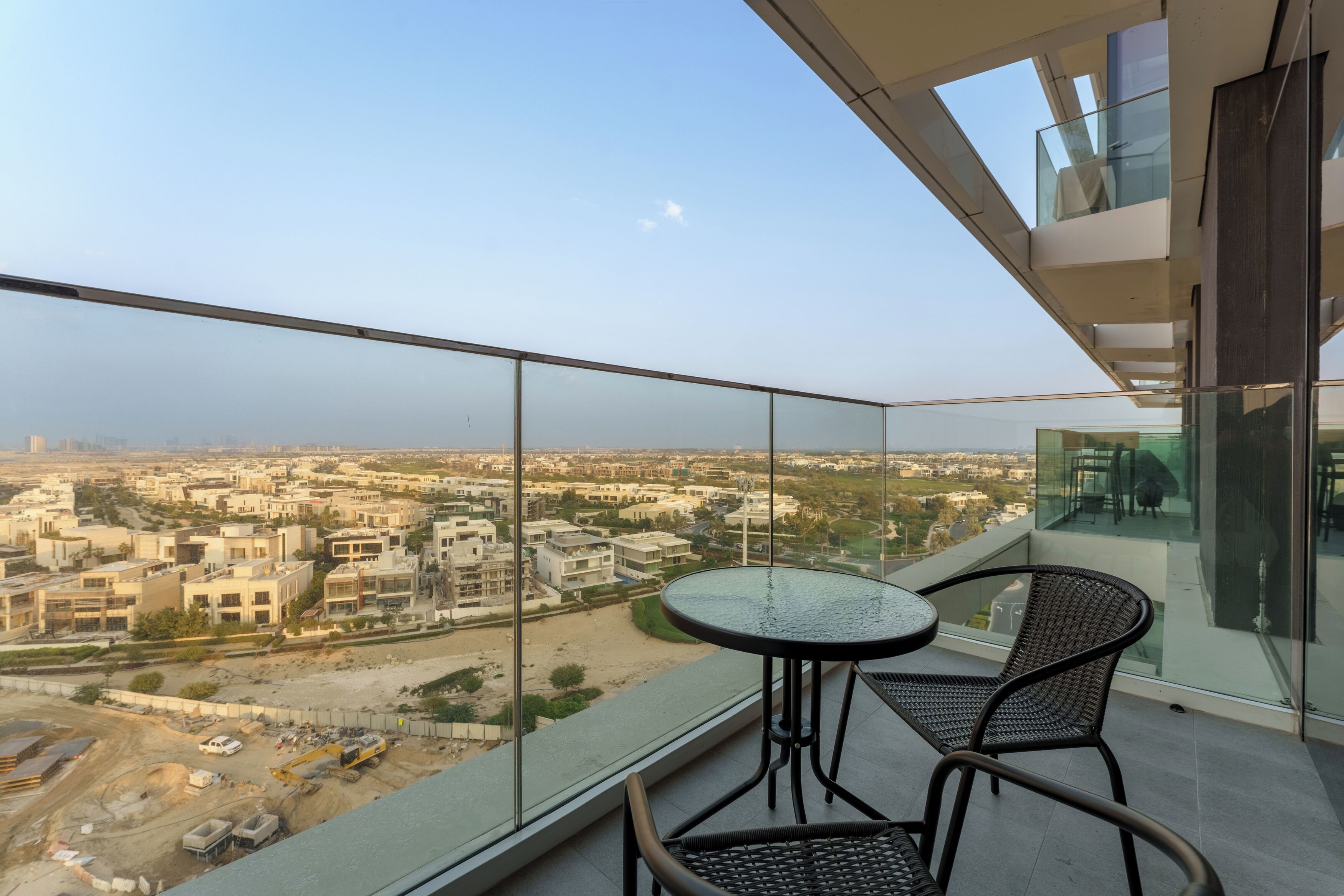A balcony with a glass railing, a round table, and two wicker chairs.