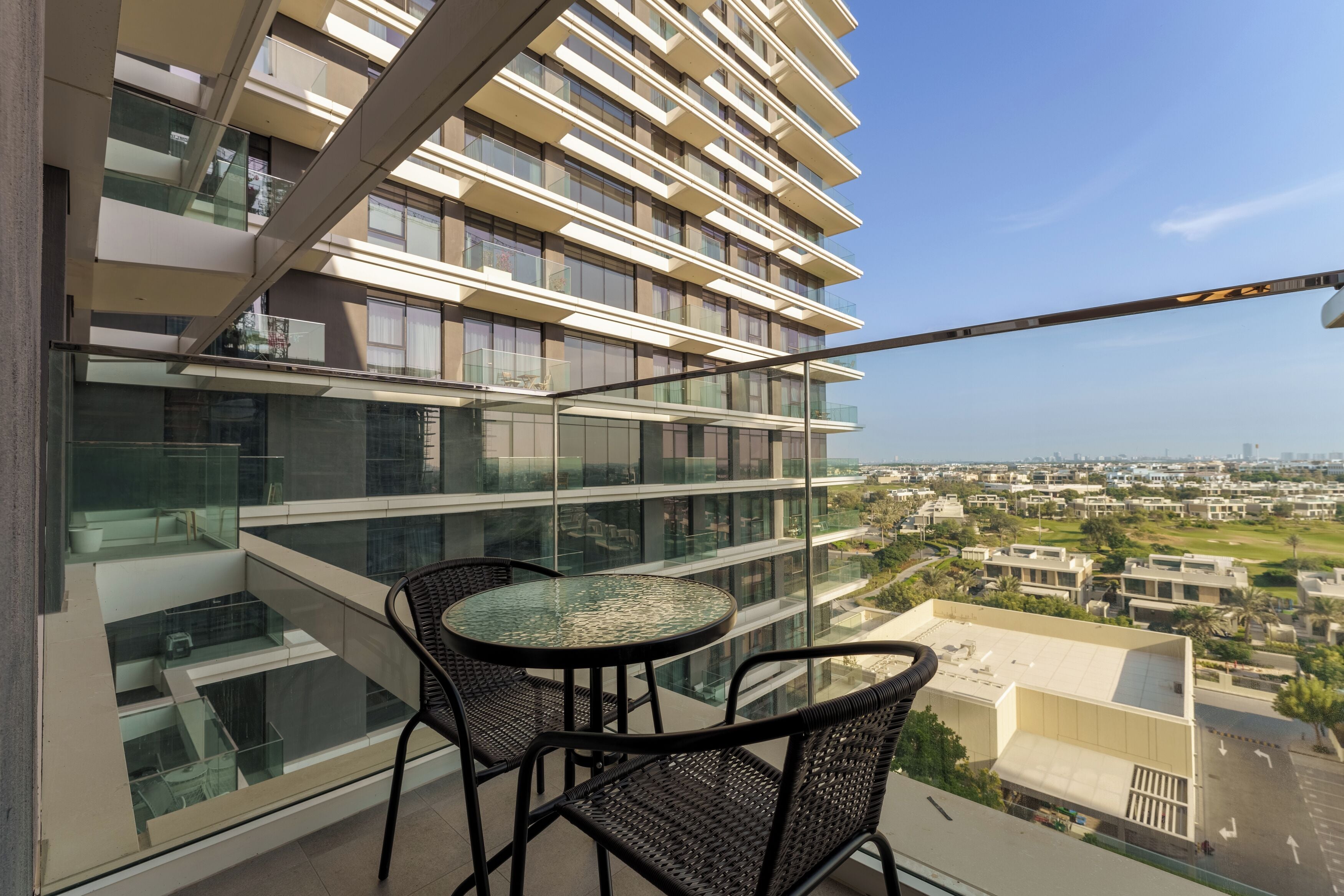 A balcony with a glass railing, two wicker chairs, and a small table.