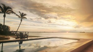 A swimming pool with a view of the sunset over a body of water, palm trees, and a distant shoreline. - Luxury River View Estate | Heated Pool & Amazing Sunsets | Perfect Gathering for Families & Friends (Fort Myers)