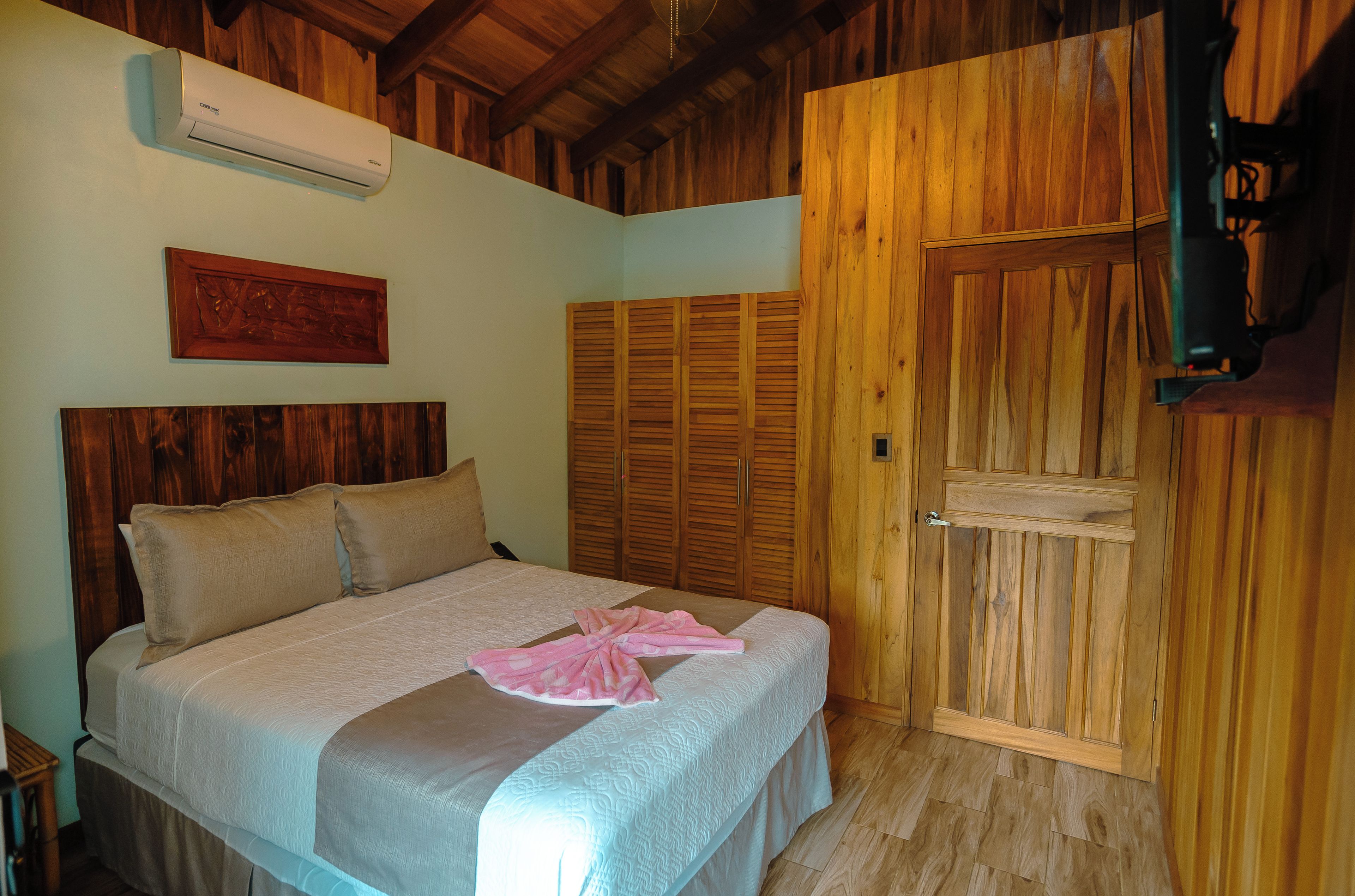 A bedroom with a bed, wooden wardrobe, and an air conditioning unit.