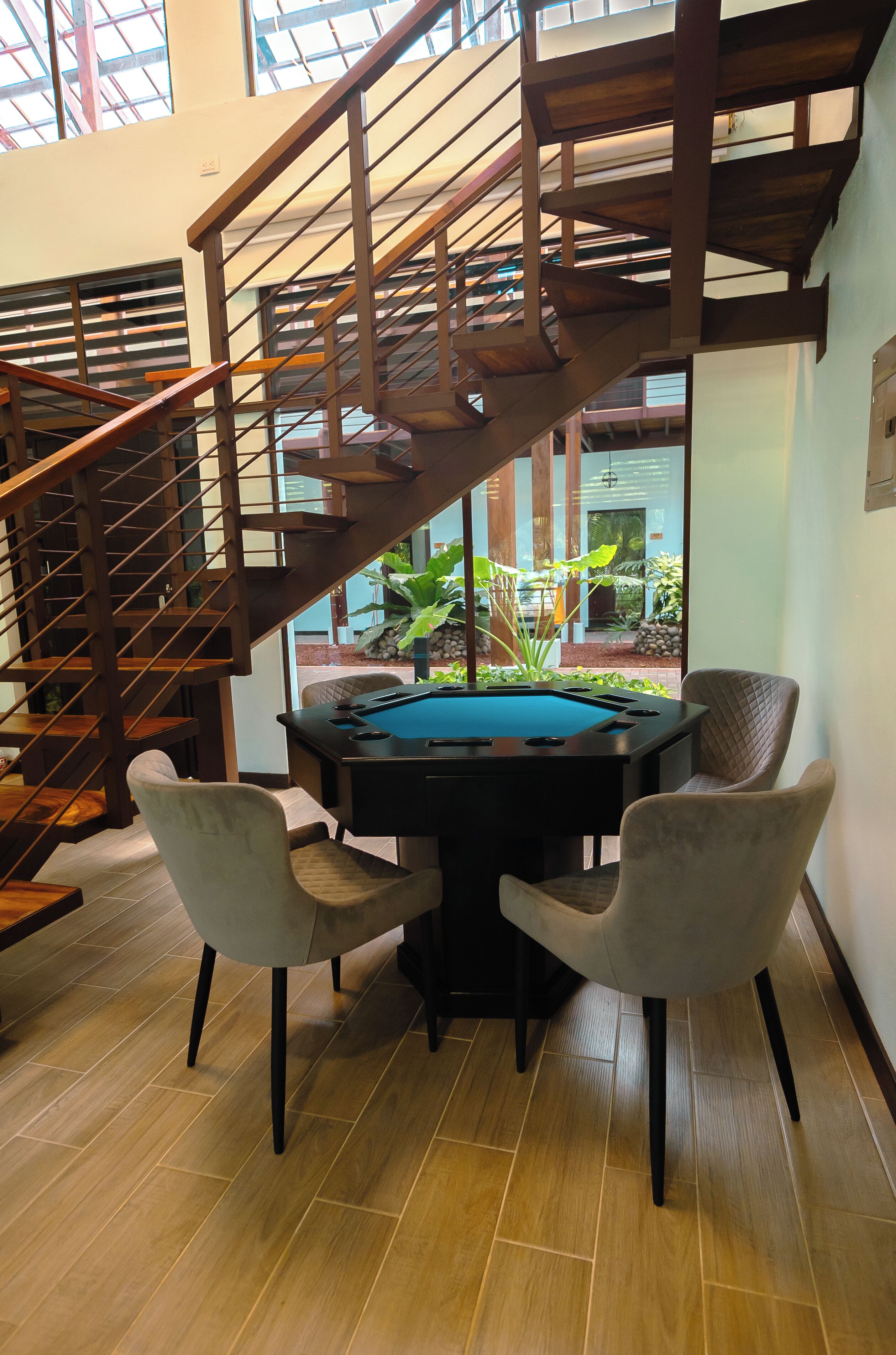 A pool table with two chairs, a wooden staircase, and a view of the outdoors.