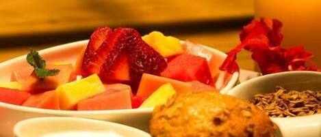 A breakfast plate with fruits, a muffin, and a glass of orange juice on a table.