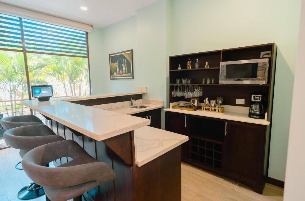 A kitchen with a bar area, bar stools, a microwave, and a shelf with glassware.