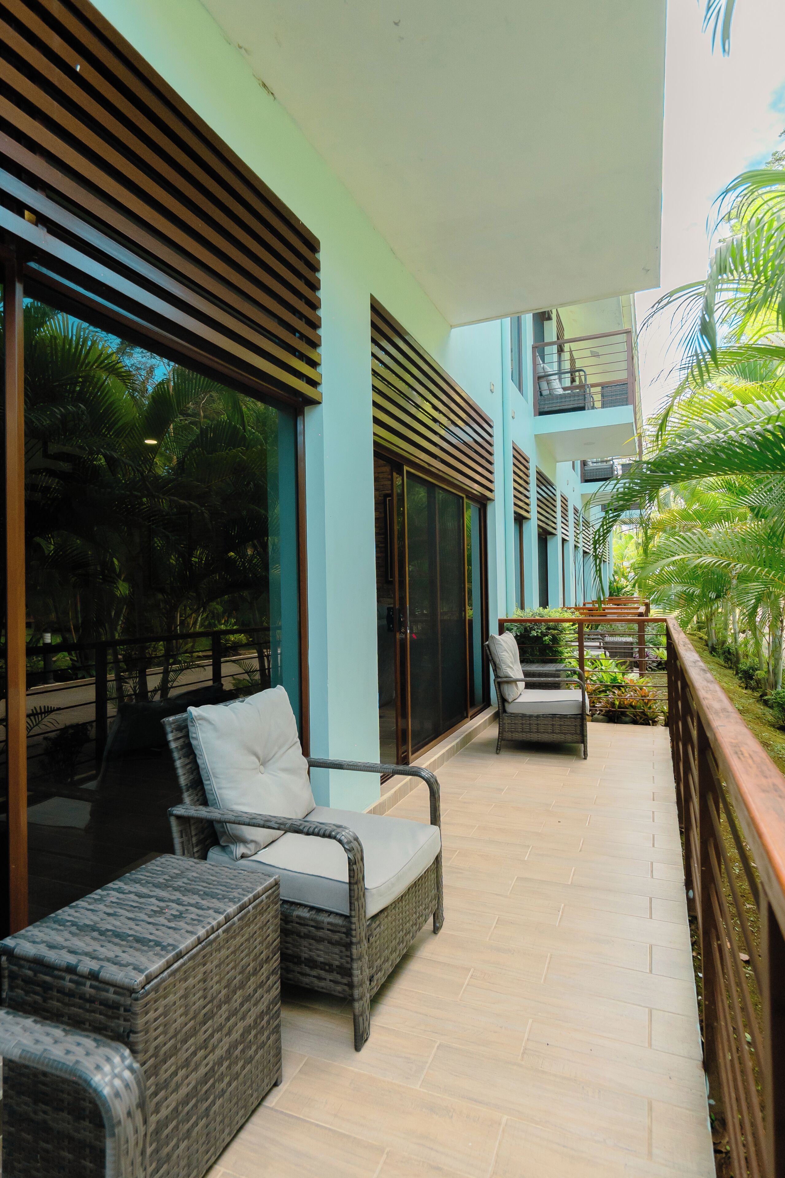 A balcony with wicker furniture, a wooden railing, and a view of a building with large windows and a balcony.