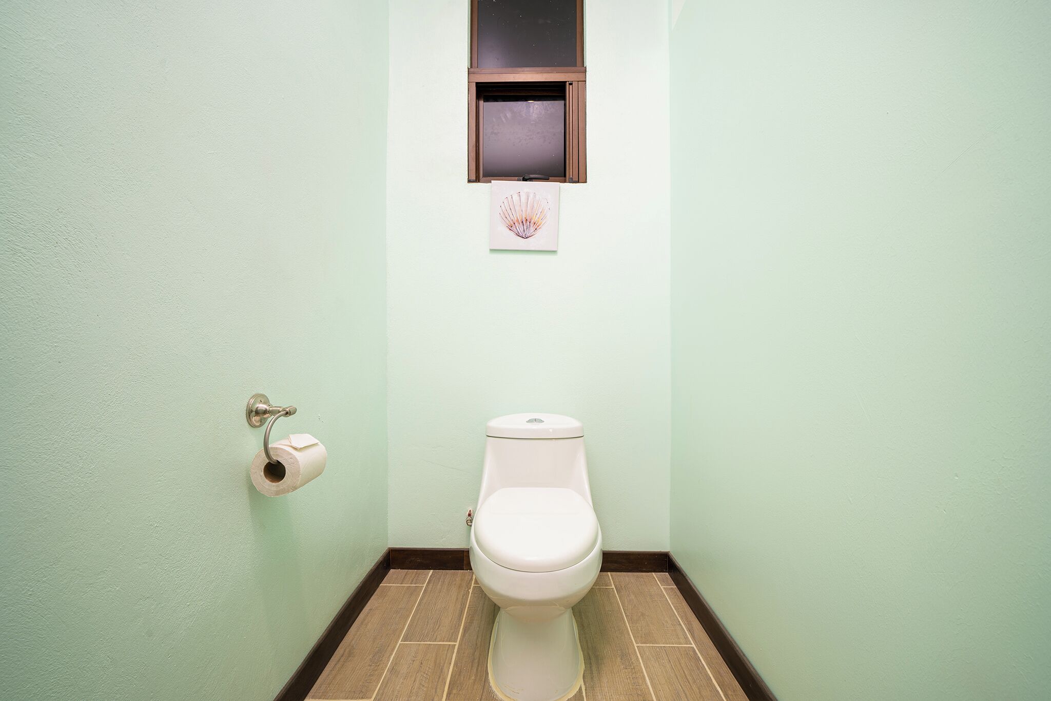 A bathroom with a toilet, a toilet paper holder, and a small window above the toilet.