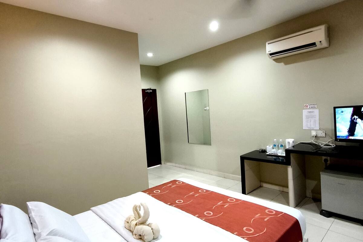 A hotel room with a bed, a desk, a TV, and an air conditioning unit.