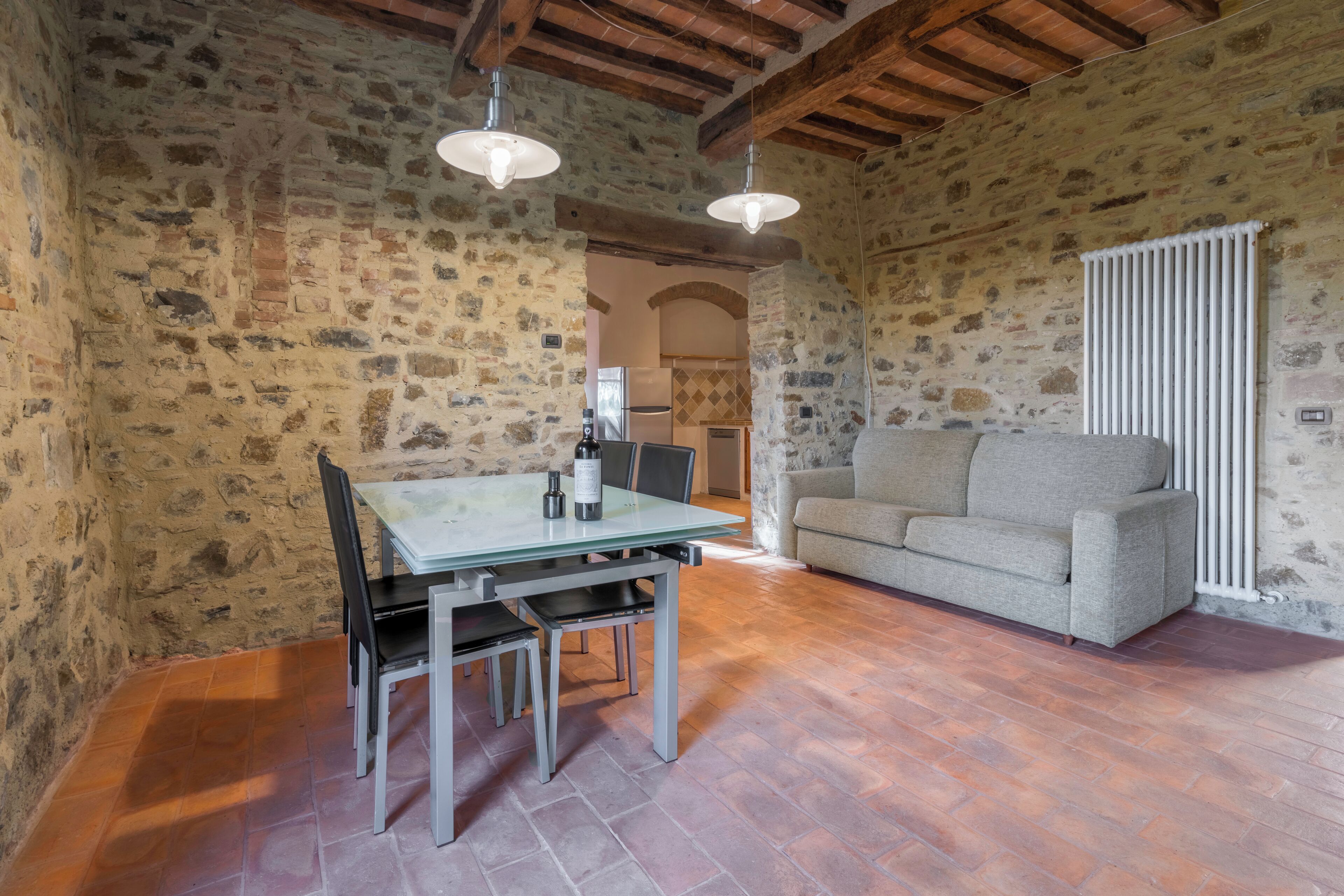 Una habitación rústica con paredes de piedra, una mesa de comedor y sillas, un sofá y un radiador.