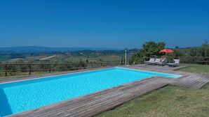 A rectangular swimming pool with a wooden deck, surrounded by a wooden fence. There are lounge chairs and a red umbrella. - Le Fonti Apartments With Ac Near Siena (Poggibonsi)