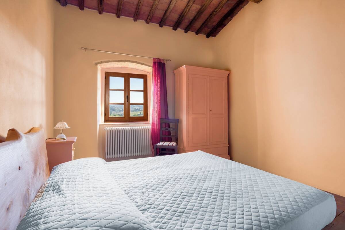 Ein Schlafzimmer mit Bett, Fenster mit Blick, Heizkörper, Kleiderschrank und Stuhl.