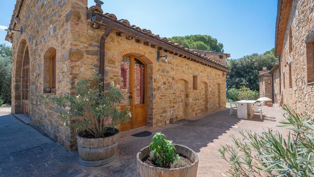 A stone building with a wooden door, potted plants, and a patio area. - Le Fonti Apartments With Ac Near Siena (Poggibonsi)
