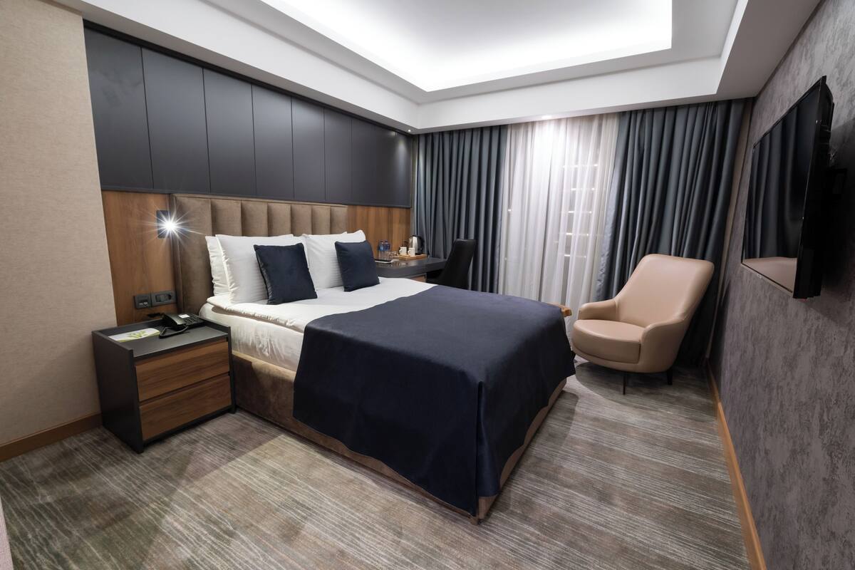 Moderni hotellihuone, jossa on suuri sänky, työpöytä, tuoli ja seinälle asennettu televisio.